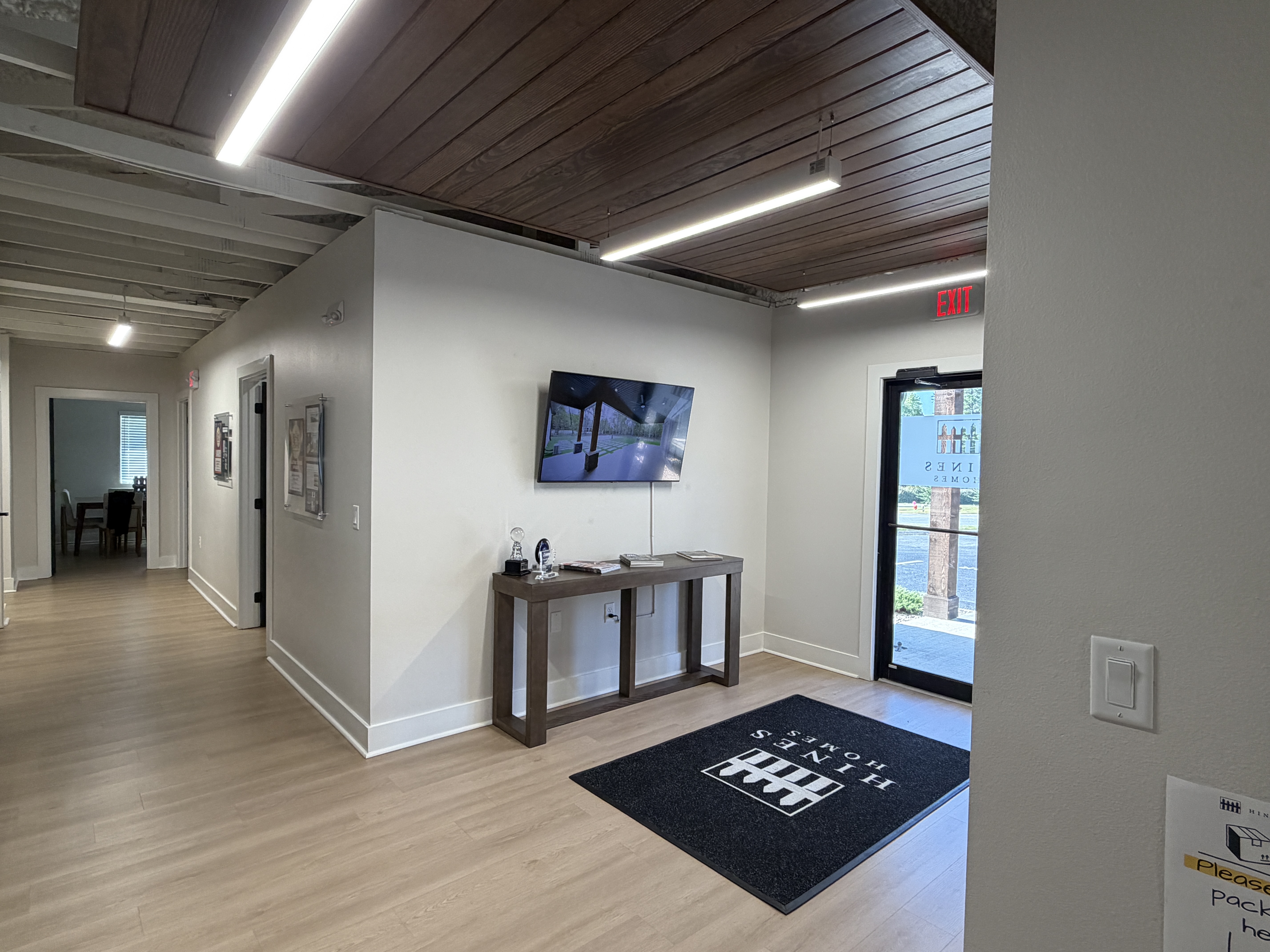 Reception area at 401 Commerce Drive with a glass-walled office, a stained plank ceiling against exposed steel joists, linear LED lighting and wood-look flooring