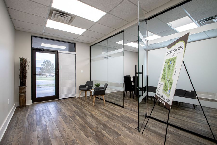 Modern office lobby with glass walls, chairs, wood flooring, and a framed sign on an easel