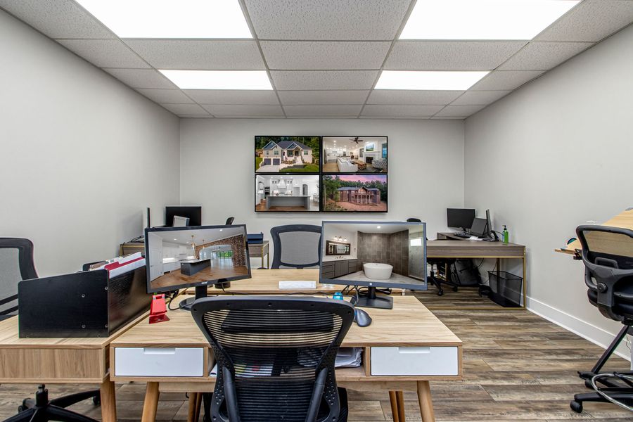 Modern office with multiple desks, computer monitors, and wall-mounted screens in a bright workspace.
