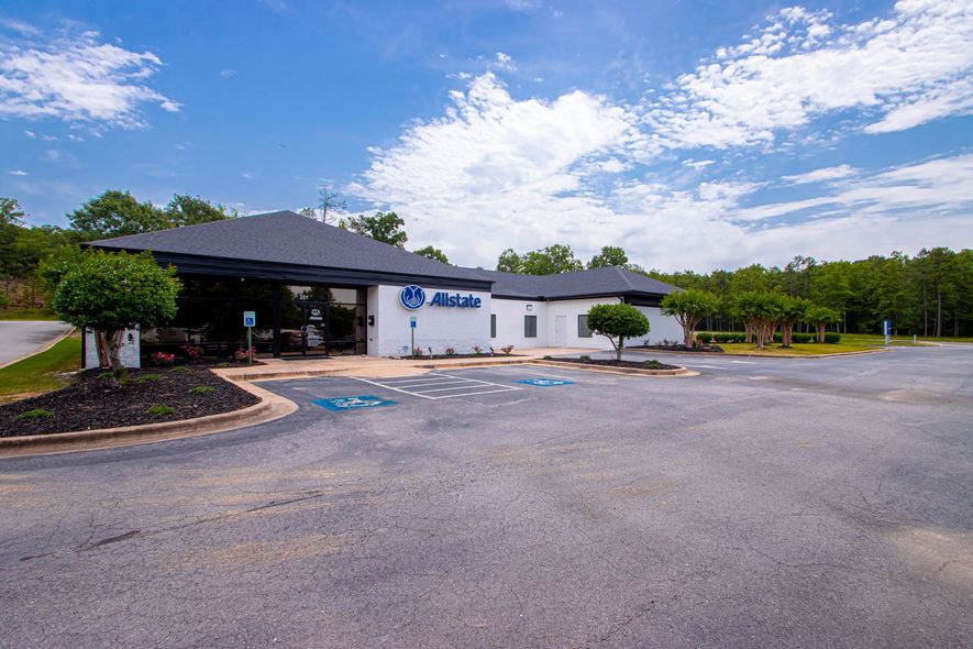 White storefront building with blue sign and empty parking lot under a partly cloudy sky