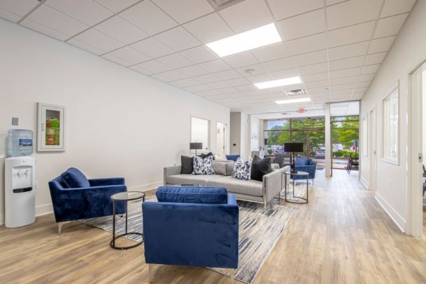 Bright modern waiting lounge with blue chairs, gray sofa, wood floors, and large windows