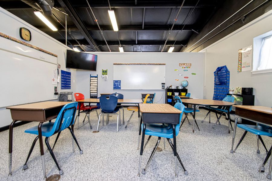 Empty classroom with blue chairs, desks, whiteboard, and TV on the front wall