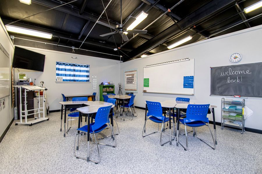 Empty classroom with blue chairs, tables, whiteboards, and a chalkboard in a bright, modern room