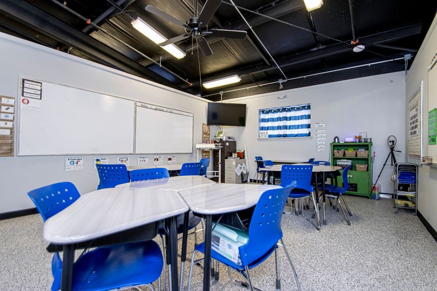 Classroom with blue chairs, white tables, whiteboard, and colorful ceiling lights