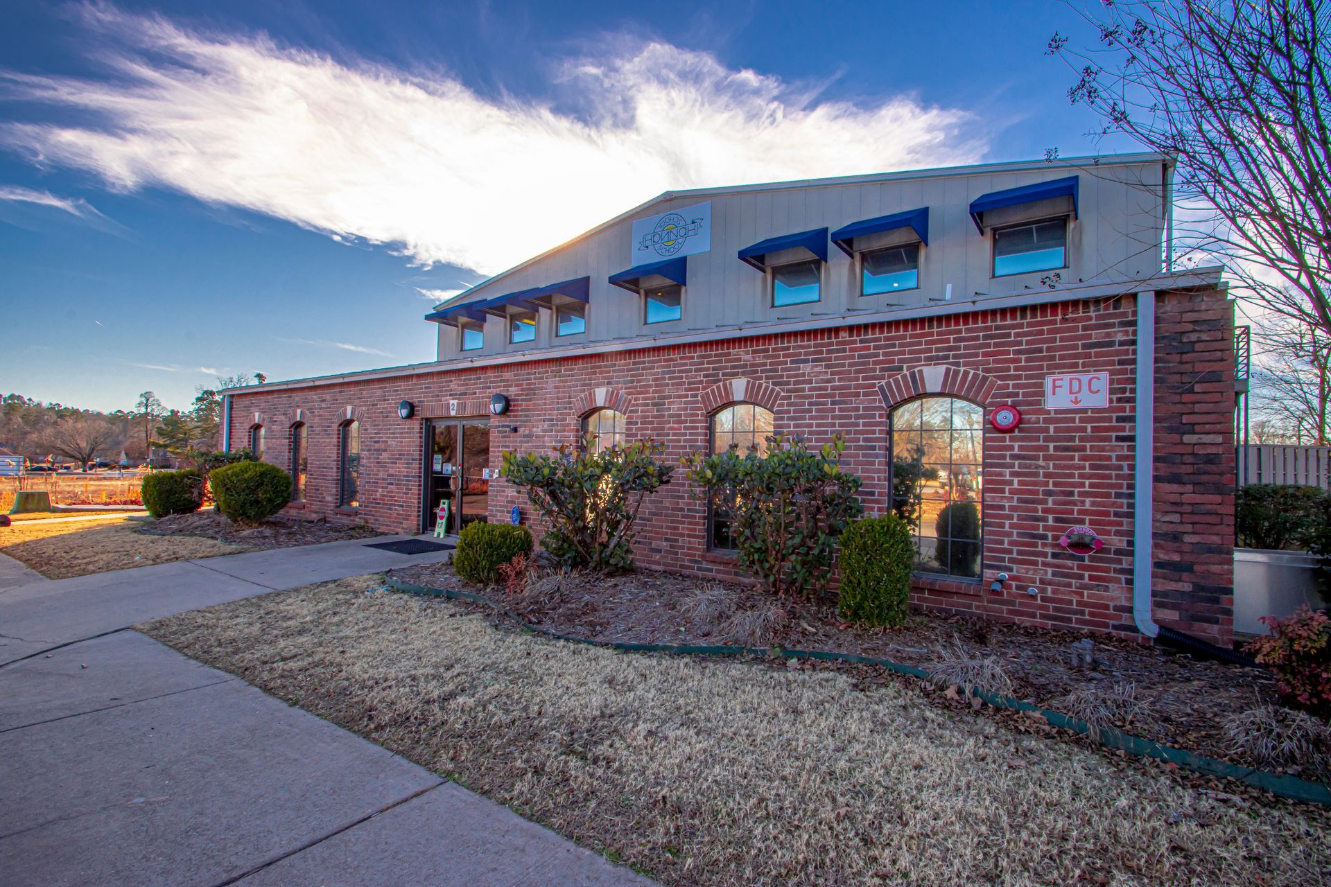 Brick building with arched windows and blue dormers beside a sidewalk under a cloudy sky