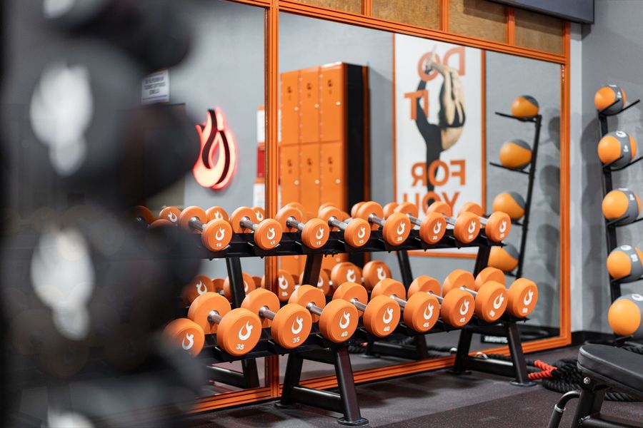 Orange dumbbells on black racks in a gym with mirrored walls and gray flooring