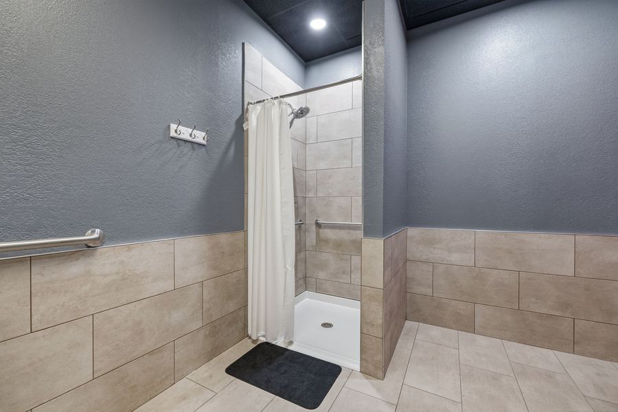Modern tiled bathroom with a shower stall, white curtain, and wall-mounted grab bar.
