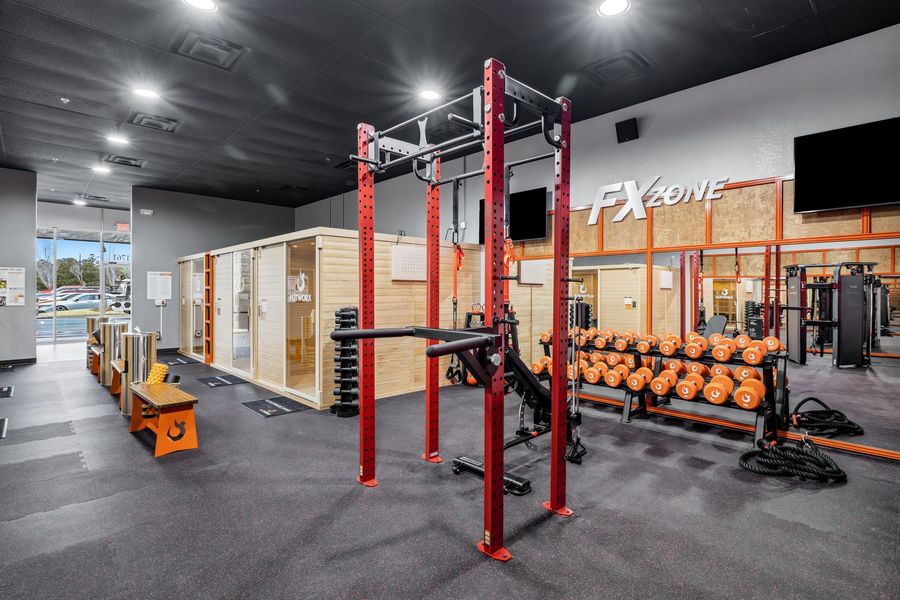 Modern gym with red power rack, dumbbells, mirrors, and benches on black flooring