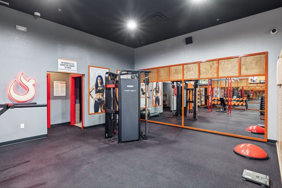Empty gym studio with mirrors, red trim, and exercise equipment on a dark carpeted floor.
