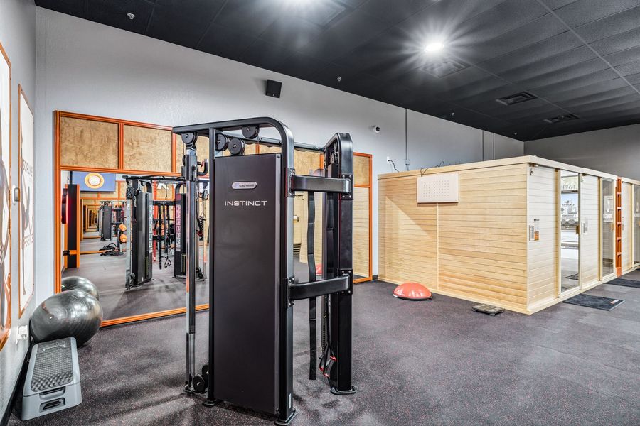 Gym with weight machines, mirrors, and a wooden saunalike room under bright ceiling lights.