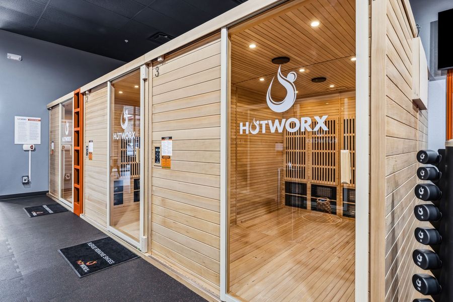 Glass-fronted sauna pods in a gym hallway, with warm wood interiors and HUTWORX branding.