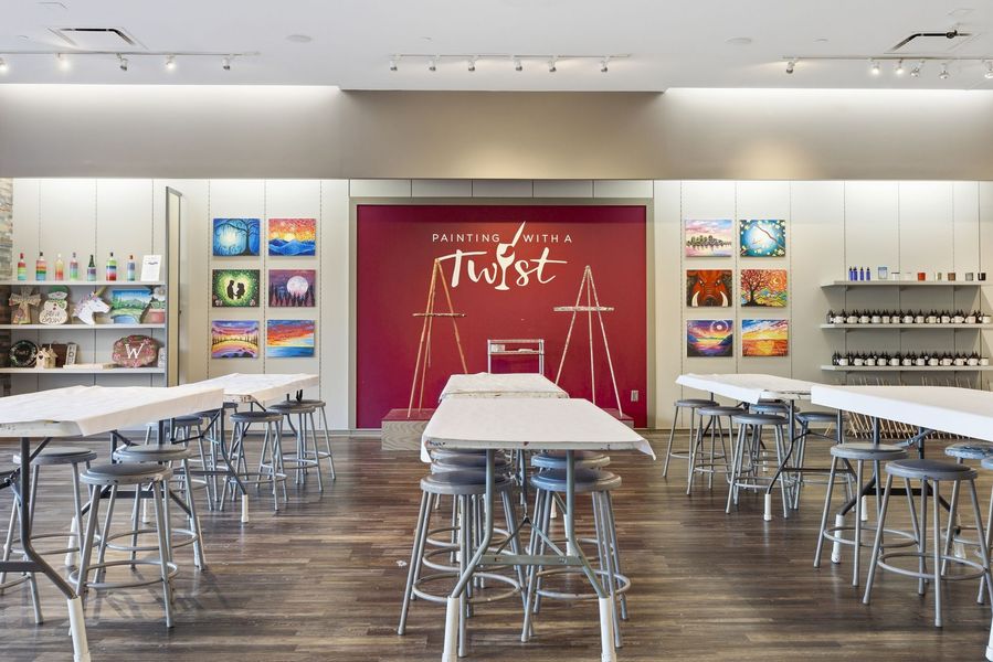 Bright cafeteria with metal tables and chairs, colorful wall art, and a red mural in the back.
