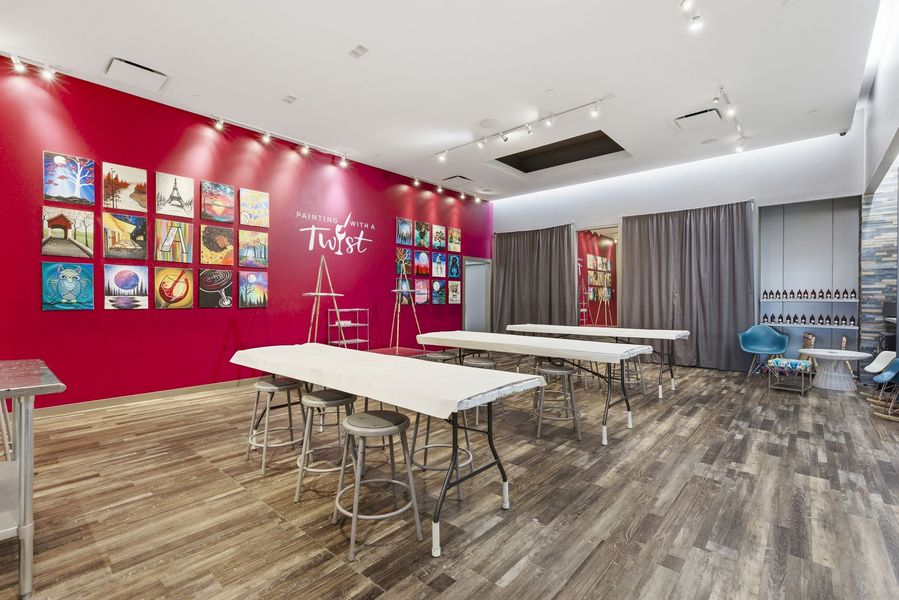 Empty classroom with white tables, stools, colorful wall art, and gray curtains on a red accent wall
