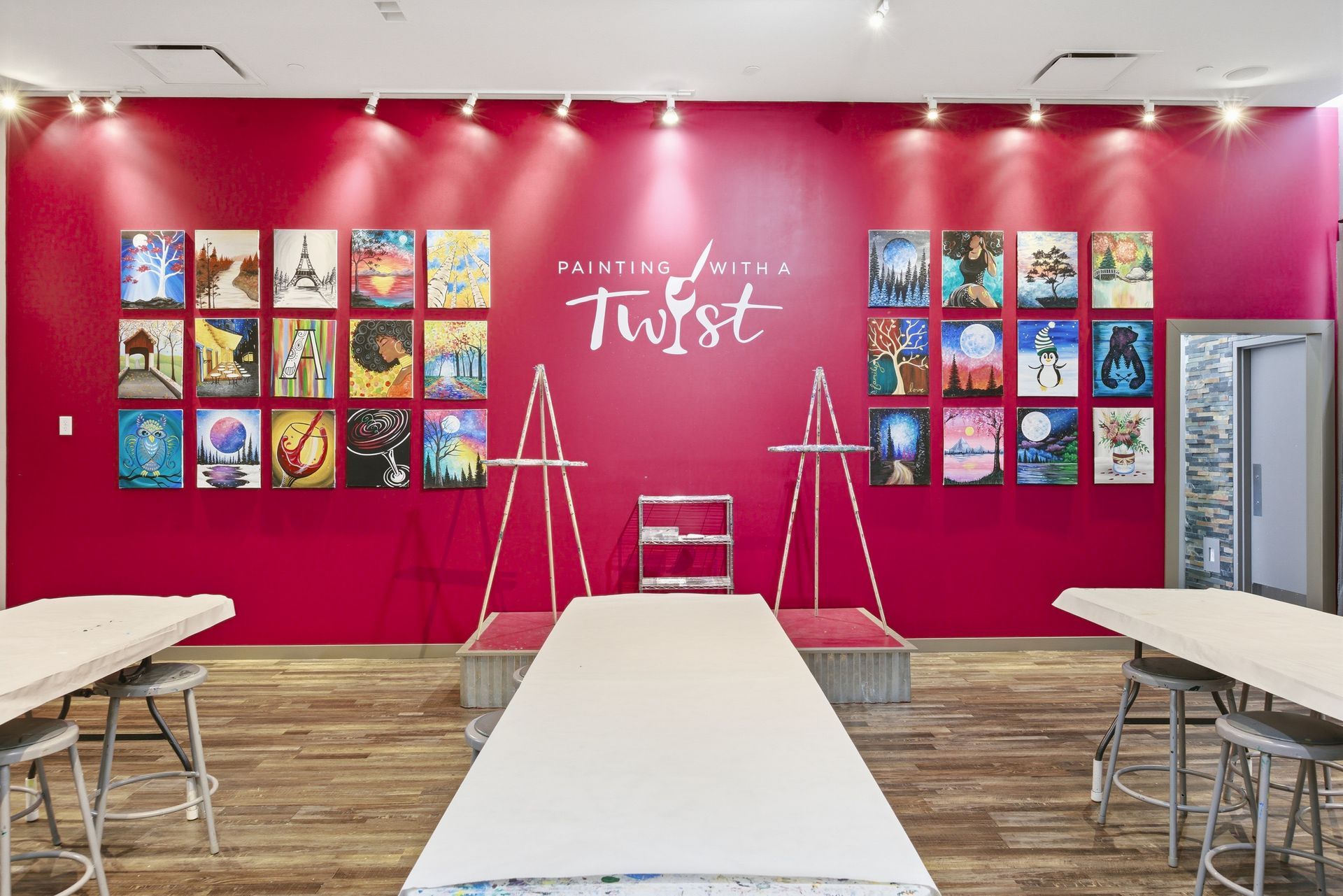 Bright pink art wall with framed colorful prints and tables in a gallery-style room